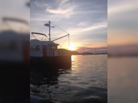 A serene sunset view of the 'Sea Tide' boat docked, reflecting the warm hues of the evening sky on calm waters — perfect for tranquil evening cruises.