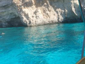 A swimmer enjoys the crystal-clear waters near a stunning rocky cave, showcasing the beauty of the destination — perfect for snorkeling and exploration.