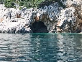 A stunning view of a rocky coastline featuring a cave, surrounded by clear turquoise waters — perfect for exploring hidden gems during a boating adventure.