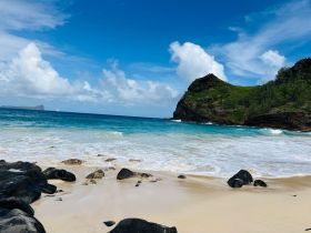 A stunning view of a secluded beach with turquoise waters and lush green hills in the background, perfect for a tropical getaway or island exploration.