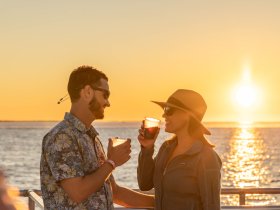 A couple enjoys cocktails while watching a stunning sunset on the water, creating the perfect romantic atmosphere for a sunset cruise.