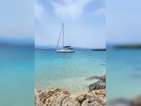 A picturesque sailboat anchored in crystal-clear waters, surrounded by stunning coastal scenery — perfect for a serene day on the water.