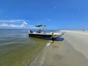 A child stands on the shore near a fishing boat, enjoying a sunny day at the beach — a perfect family outing for fishing and fun in the sun.