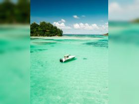 An aerial view of a boat anchored in stunning turquoise waters near a lush island, showcasing the beauty of a tropical getaway.