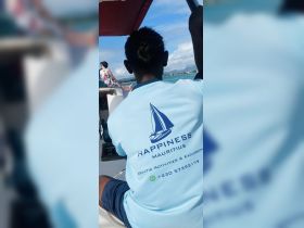 A crew member in a blue shirt promotes aquatic activities in Mauritius while steering the boat, showcasing the vibrant marine environment.