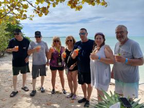 A cheerful group enjoys cocktails on the beach, celebrating together in a picturesque setting — perfect for memorable gatherings and fun in the sun.
