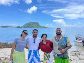 A cheerful group poses on the beach with a stunning island backdrop, capturing a memorable moment during their tropical adventure.