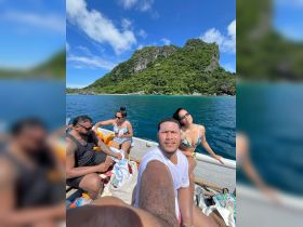 A lively group enjoys a sunny day on a boat, capturing memories with stunning island scenery in the background — perfect for adventure and celebration.