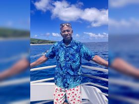 A man poses on the deck of a boat against a stunning ocean backdrop, showcasing the perfect tropical getaway experience.