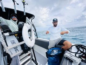 Two individuals are aboard a fishing boat, engaged in activities on the water, showcasing the excitement of a fishing trip.