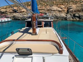 A stunning view of the deck of a yacht, showcasing its spacious seating area against a backdrop of crystal-clear waters and rocky cliffs, perfect for relaxing on a sunny day.