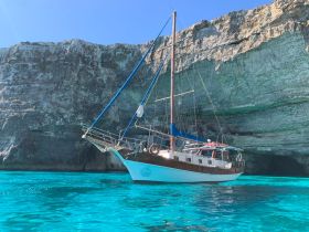 A beautiful sailboat anchored near stunning cliffs, surrounded by crystal-clear turquoise waters — an ideal setting for sailing adventures.