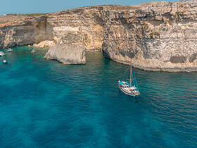 A stunning aerial view of a sailboat anchored near dramatic cliffs, surrounded by crystal-clear turquoise waters — perfect for exploring coastal landscapes.