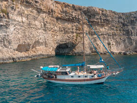A group of guests enjoys a day on a beautiful boat near a stunning coastline, perfect for swimming and adventure on the water.