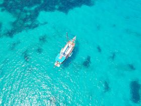 A stunning aerial view of a yacht cruising through crystal-clear turquoise waters, showcasing the beauty of the ocean and the vessel's elegant design.