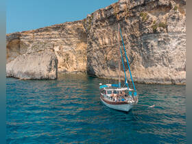 A picturesque scene featuring a boat anchored near stunning cliffs, with guests enjoying a swim in the crystal-clear waters — a perfect highlight of a summer adventure.