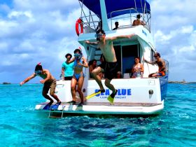 A lively group enjoys snorkeling from a luxury yacht, with one person jumping into the crystal-clear waters — a perfect moment for adventure seekers.