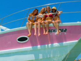 A group of friends enjoys a sunny day on the bow of a pink boat, capturing the essence of summer fun and celebration on the water.