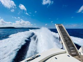 A stunning view from the back of a boat as it speeds through the open water, showcasing the beautiful blue sea and distant coastline.