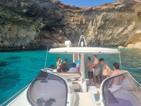 A lively group enjoys a sunny day on a boat near stunning cliffs, perfect for swimming and relaxation in crystal-clear waters.