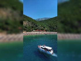 A lively scene featuring a boat named 'Montenegro II' with guests enjoying the sun and water, set against a picturesque beach backdrop in Montenegro.