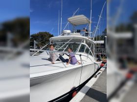 Two children happily pose on the deck of a boat at the dock, showcasing a fun family outing on the water.