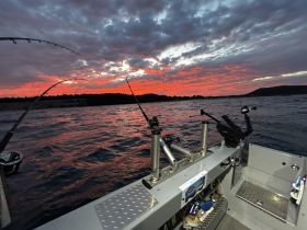 A stunning sunset view from a fishing boat, with rods ready for action against a vibrant sky — perfect for evening fishing adventures.