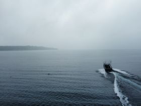 Aerial view of a fishing boat navigating through calm waters under a cloudy sky, showcasing the serene beauty of a maritime adventure.