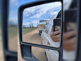 A boat is being towed down a dirt road, captured in the side mirror of a pickup truck — a common sight for boating enthusiasts preparing for a day on the water.