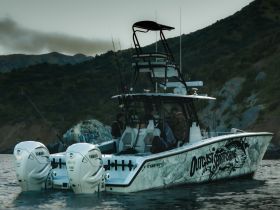 A fishing boat named 'Outcast Sportfishing' is anchored in serene waters, with anglers preparing for a day of adventure amidst stunning coastal scenery.