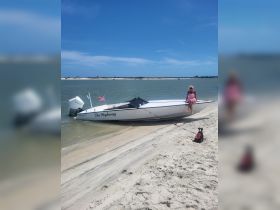 A woman relaxes on the beach next to 'The Highway' boat, accompanied by her dog, enjoying a sunny day by the water.