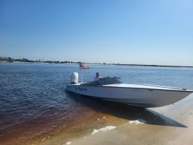 A sleek speedboat named 'The Highway' is docked on a sandy shore, showcasing its stylish design against a clear blue sky.