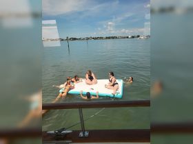 A lively group enjoys a fun day on a floating mat in the water, perfect for summer parties and relaxation under the sun.