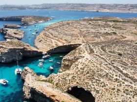 A stunning aerial view of a picturesque coastline with multiple boats anchored in turquoise waters, showcasing the natural beauty of the islands.
