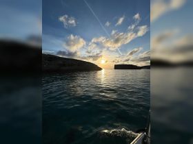 A stunning sunset view over calm waters, showcasing the coastline and creating a perfect backdrop for serene boating experiences.
