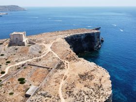 A stunning aerial view of a rugged coastline with clear blue waters, showcasing the natural beauty of the landscape — perfect for exploring by boat.