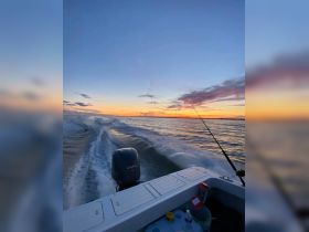 A stunning sunset view from a fishing boat, capturing the serene beauty of the water as the boat leaves a wake behind — perfect for evening fishing trips.