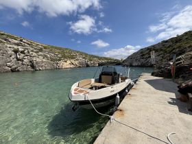 A sleek speedboat docked in a serene cove, surrounded by rocky cliffs and clear turquoise waters — an ideal spot for a day of relaxation on the water.