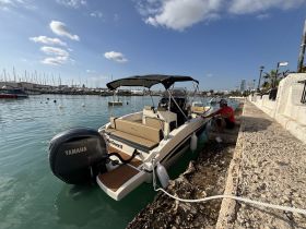 A sleek speedboat named 'Mia Grace II' docked at the marina, with a person preparing it for the day. The vibrant waters and surrounding boats create a picturesque setting.