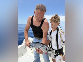 A father and son proudly display their catch while fishing on the open ocean, capturing a memorable moment of adventure and bonding on the water.