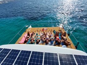 A lively group enjoys sunbathing on the deck of a catamaran, surrounded by stunning turquoise waters — perfect for a fun day on the water.