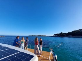 A lively group enjoys a sunny day on the boat, with some swimming in the clear blue waters — perfect for a fun day out at sea.
