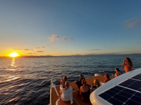 A group of friends enjoys a stunning sunset aboard a yacht, capturing the moment with drinks in hand — perfect for memorable celebrations on the water.