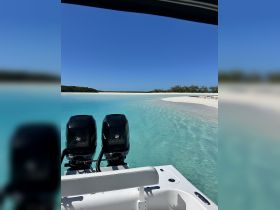 A clear view of a boat's outboard motors with stunning turquoise waters and a sandy beach in the background, perfect for showcasing boating adventures in tropical destinations.