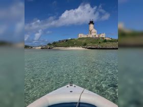 A stunning view from a boat towards a historic lighthouse on an island, surrounded by crystal-clear waters — perfect for exploring scenic coastal destinations.