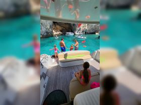 A family enjoys a fun day on the water, with kids swimming and playing near the boat in a beautiful turquoise cove.
