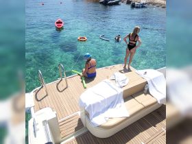 Guests enjoy a sunny day on the water, with one person swimming and another relaxing on the boat — perfect for summer adventures and water activities.