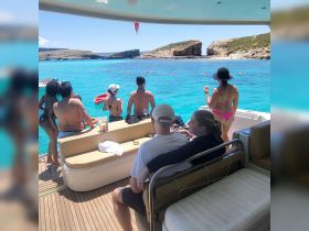 A lively group enjoys a sunny day on a pontoon boat, taking in the stunning turquoise waters and rocky coastline — perfect for a fun-filled beach day.
