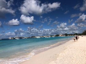 A picturesque beach scene with people strolling along the shore, surrounded by turquoise waters and anchored boats in the background — a perfect destination for relaxation and exploration.