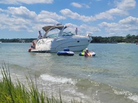 A lively group enjoys a sunny day on the water, with some relaxing on inflatable tubes while others are on the boat — perfect for summer fun and family outings.